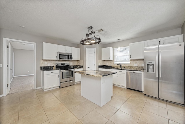 kitchen with light tile patterned flooring, white cabinets, appliances with stainless steel finishes, decorative light fixtures, and a kitchen island