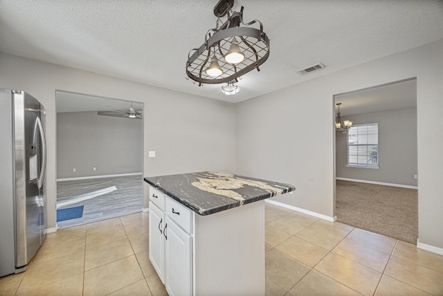 kitchen featuring dark stone counters, light tile patterned floors, decorative light fixtures, stainless steel fridge with ice dispenser, and white cabinetry