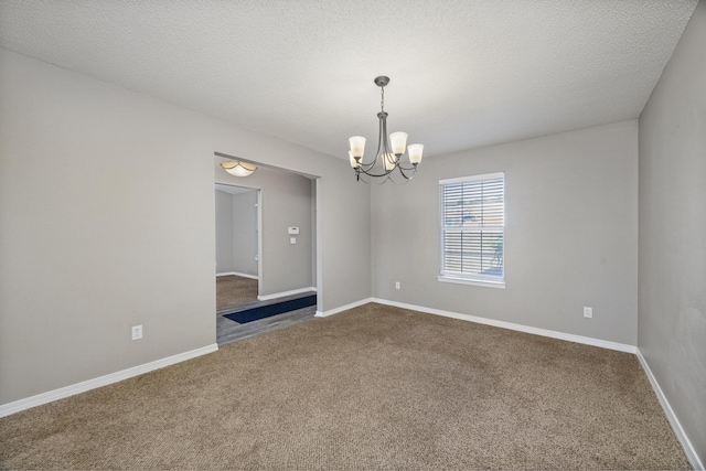 carpeted empty room featuring a textured ceiling and a notable chandelier