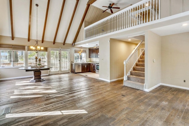 unfurnished living room featuring ceiling fan with notable chandelier, hardwood / wood-style flooring, high vaulted ceiling, and plenty of natural light