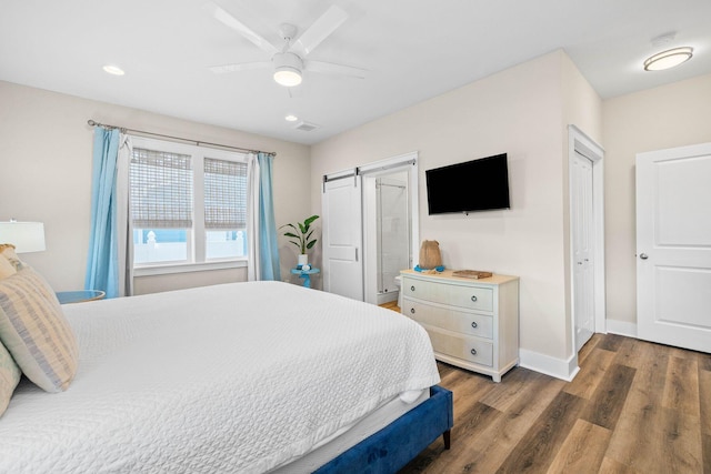 bedroom with dark hardwood / wood-style floors, a barn door, and ceiling fan