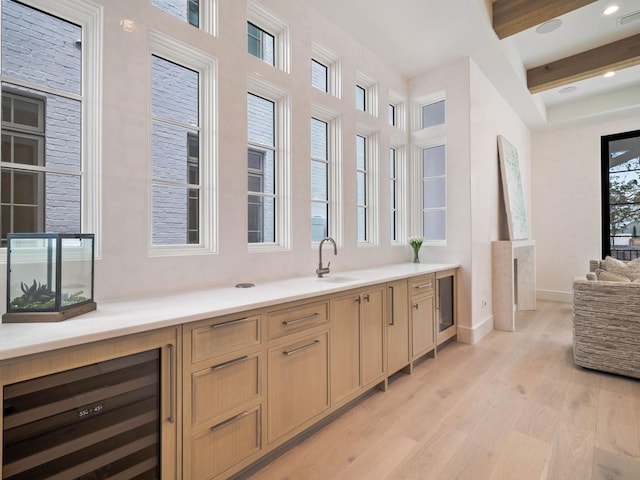 bar with light brown cabinets, sink, wine cooler, beamed ceiling, and light hardwood / wood-style floors