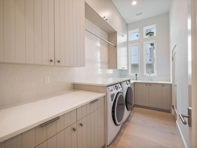 washroom with cabinets, washing machine and dryer, light hardwood / wood-style flooring, and sink