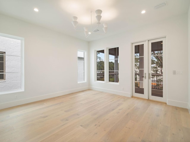 empty room with a chandelier, french doors, and light hardwood / wood-style flooring