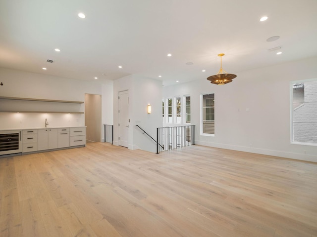 unfurnished living room with light hardwood / wood-style floors, sink, and wine cooler