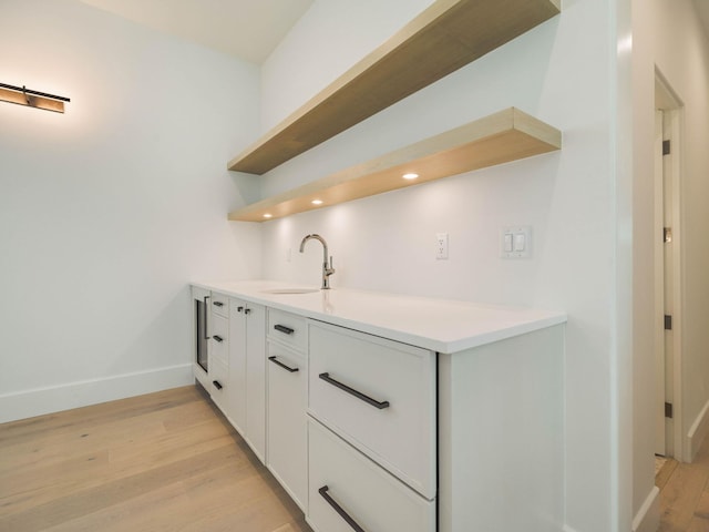 bar with white cabinetry, sink, and light hardwood / wood-style flooring