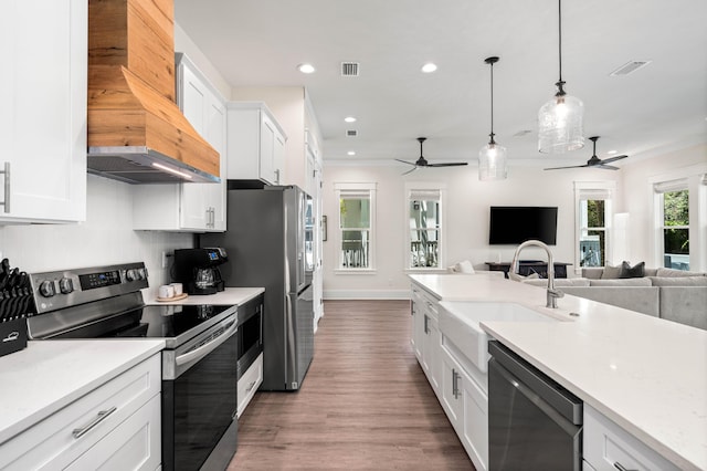 kitchen featuring custom range hood, stainless steel appliances, pendant lighting, hardwood / wood-style flooring, and white cabinetry