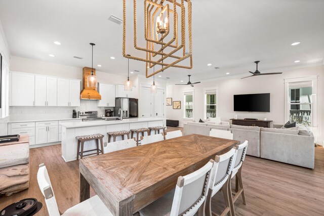 dining area with ceiling fan with notable chandelier, light hardwood / wood-style floors, and a healthy amount of sunlight