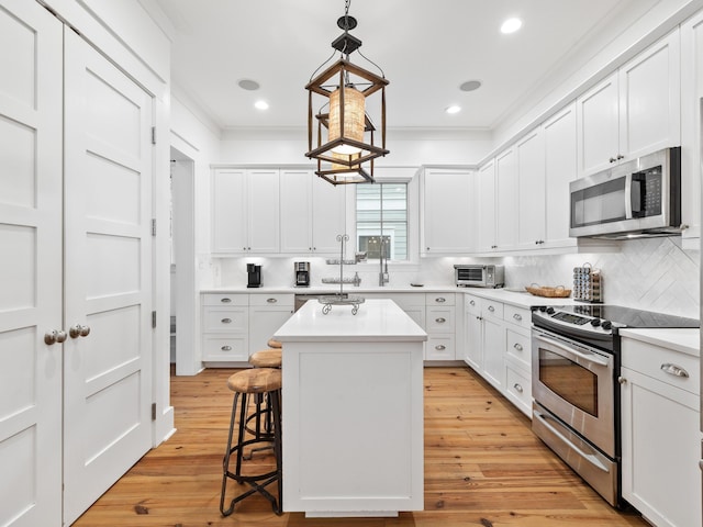 kitchen with appliances with stainless steel finishes, ornamental molding, a kitchen island, light wood-type flooring, and a kitchen bar