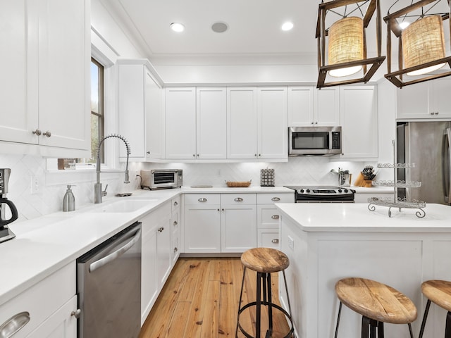 kitchen with stainless steel appliances, a breakfast bar, white cabinets, light countertops, and crown molding