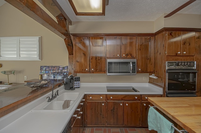 kitchen with stovetop, oven, a textured ceiling, and sink