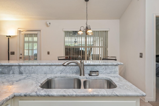 kitchen with light stone countertops, sink, pendant lighting, and a notable chandelier