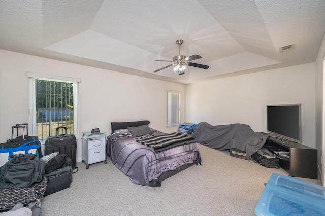 bedroom with a raised ceiling, ceiling fan, light carpet, and a textured ceiling