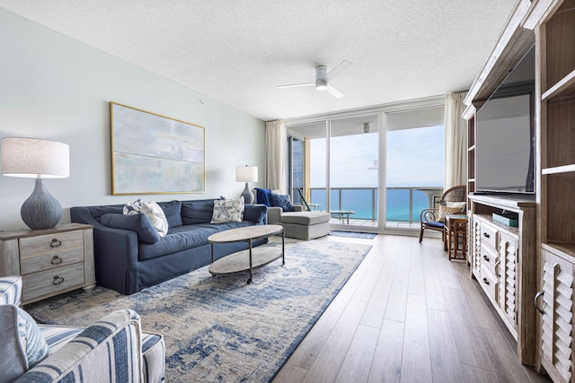 living area with a water view, floor to ceiling windows, wood finished floors, a textured ceiling, and a ceiling fan