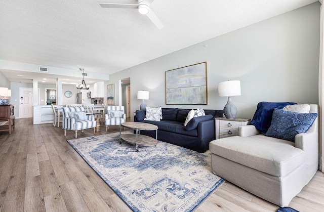 living room with light wood finished floors, visible vents, ceiling fan with notable chandelier, and a textured ceiling