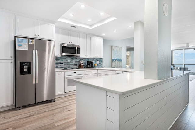 kitchen with a peninsula, light wood-style flooring, stainless steel appliances, light countertops, and a raised ceiling