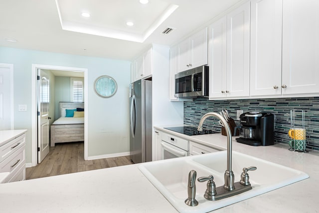 kitchen featuring a sink, a tray ceiling, white cabinetry, stainless steel appliances, and light countertops