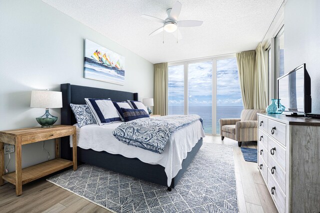 bedroom featuring ceiling fan, floor to ceiling windows, wood finished floors, and a textured ceiling