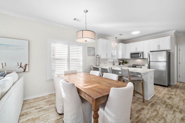 dining room with light hardwood / wood-style floors, ornamental molding, and sink