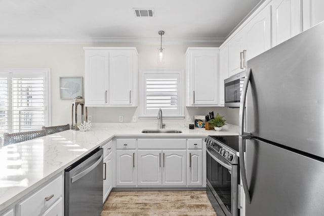 kitchen featuring appliances with stainless steel finishes, light stone counters, sink, decorative light fixtures, and white cabinets