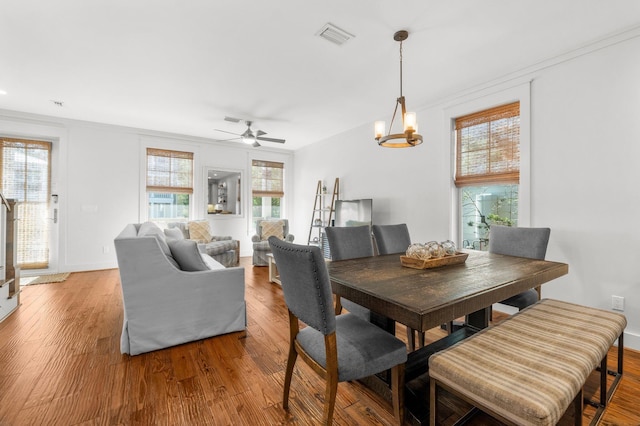 dining area featuring hardwood / wood-style floors, ceiling fan with notable chandelier, and crown molding