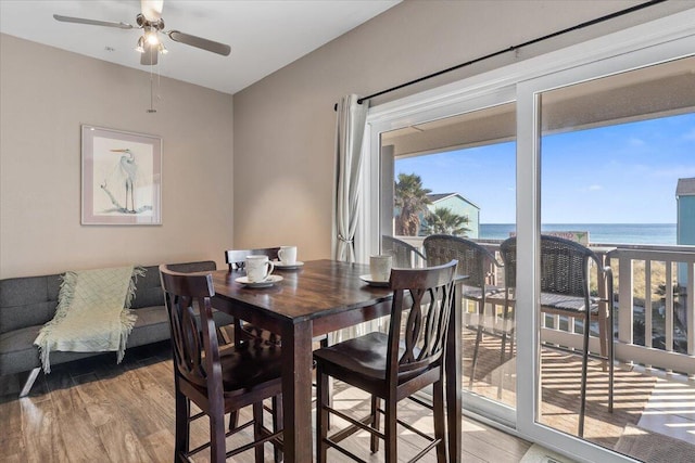 dining area with ceiling fan, a water view, and wood-type flooring