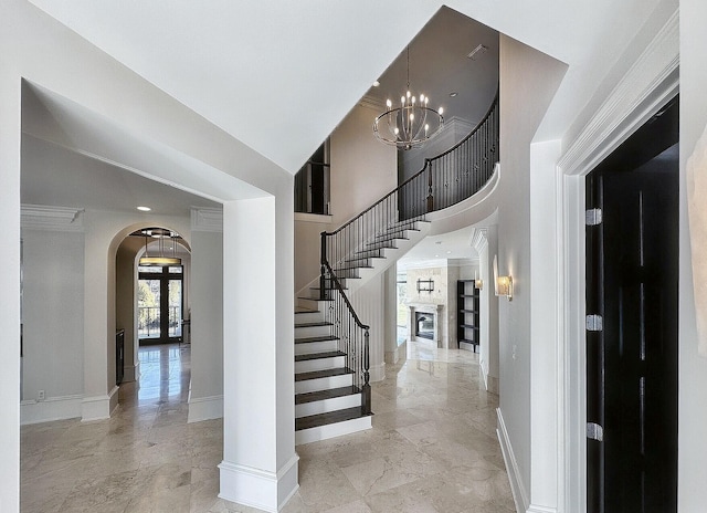 stairs featuring a large fireplace, a high ceiling, crown molding, an inviting chandelier, and french doors