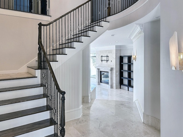 staircase with a towering ceiling, a fireplace, and ornamental molding