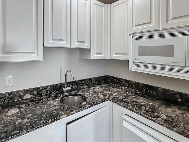 kitchen featuring white cabinetry, sink, white microwave, and dark stone counters