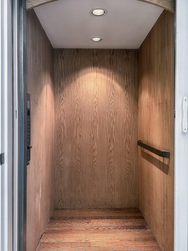 interior space with hardwood / wood-style flooring, elevator, and wooden walls