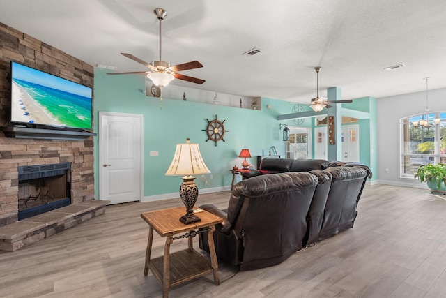 living room with ceiling fan with notable chandelier, a textured ceiling, a stone fireplace, french doors, and light hardwood / wood-style flooring