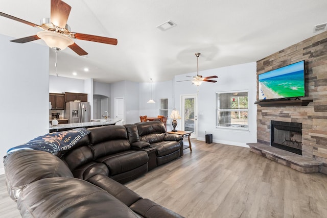 living room featuring light wood-type flooring, ceiling fan, and a fireplace