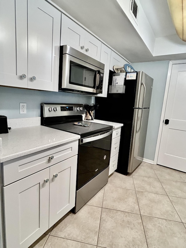 kitchen featuring white cabinets, light stone countertops, light tile patterned floors, and appliances with stainless steel finishes