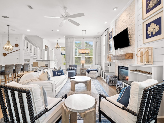 living room with hardwood / wood-style flooring, ceiling fan with notable chandelier, a stone fireplace, and ornamental molding