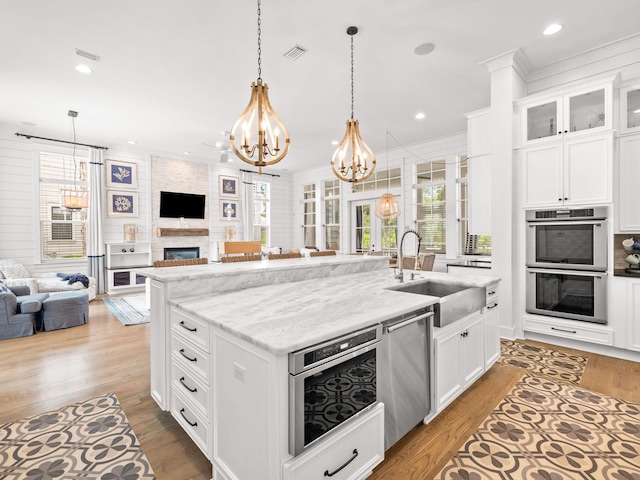 kitchen with a fireplace, stainless steel appliances, sink, white cabinets, and an island with sink