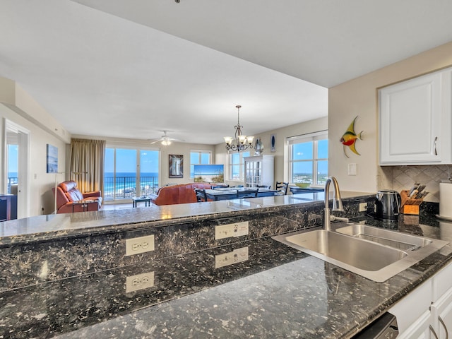 kitchen featuring sink, tasteful backsplash, dark stone countertops, white cabinets, and ceiling fan with notable chandelier