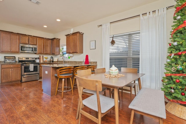 kitchen featuring dark wood-type flooring, stone counters, a kitchen breakfast bar, appliances with stainless steel finishes, and kitchen peninsula