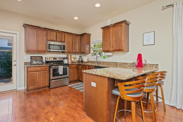 kitchen featuring kitchen peninsula, light stone countertops, stainless steel appliances, dark hardwood / wood-style floors, and a breakfast bar area