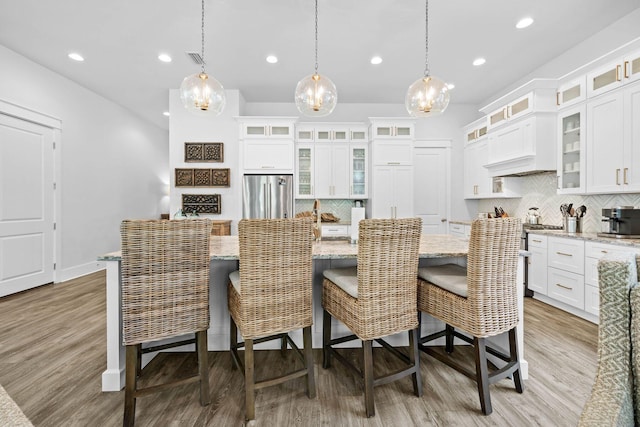 kitchen featuring a breakfast bar, white cabinets, stainless steel fridge, decorative light fixtures, and a kitchen island