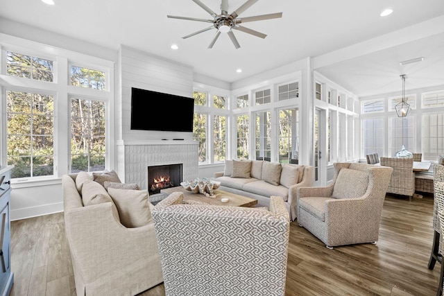 living room featuring hardwood / wood-style flooring, ceiling fan, and a large fireplace