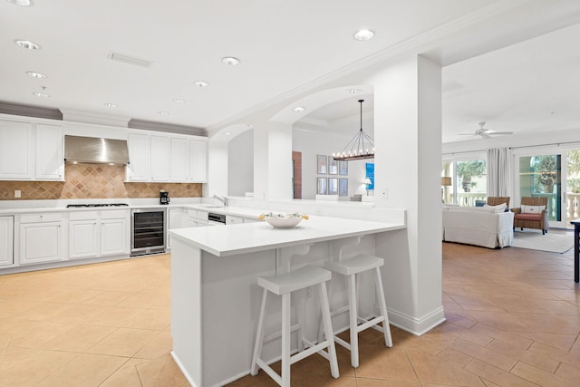 kitchen with kitchen peninsula, white cabinetry, wall chimney exhaust hood, and beverage cooler