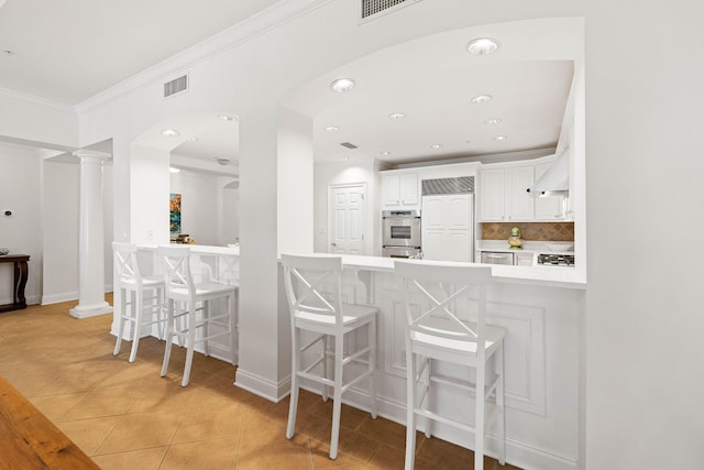 kitchen with light tile patterned floors, kitchen peninsula, a breakfast bar area, decorative backsplash, and white cabinets