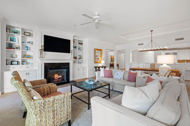 tiled living room with built in shelves, ceiling fan with notable chandelier, and crown molding