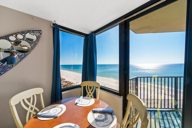 dining space with a beach view, a textured ceiling, and a water view