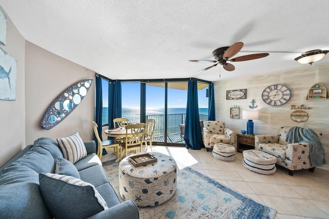 living room with a textured ceiling, a water view, expansive windows, and ceiling fan