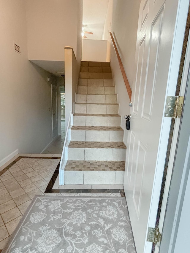 stairs with a ceiling fan, a high ceiling, visible vents, and baseboards