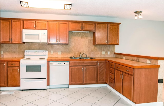 kitchen featuring a peninsula, white appliances, a sink, light countertops, and brown cabinets