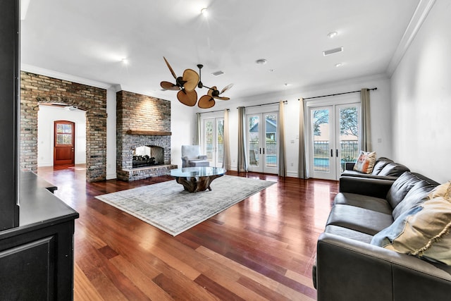 living room with french doors, dark wood-type flooring, a brick fireplace, and crown molding