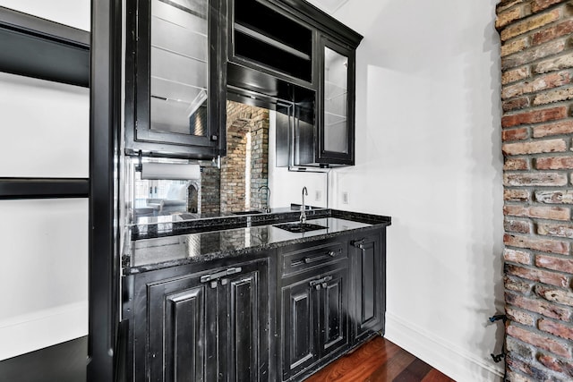 kitchen with dark hardwood / wood-style floors, brick wall, sink, and dark stone counters