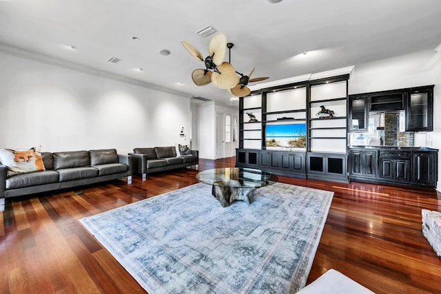 living room with built in shelves, dark hardwood / wood-style flooring, ceiling fan, and ornamental molding